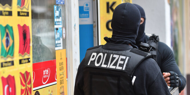 Vermummte Einsatzkräfte stehen vor einem Kiosk im Stadtteil Berlin-Neukölln