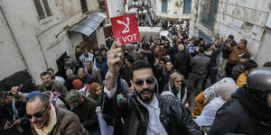 Ein Demonstrant hält vor einer Menschenmenge ein rotes Schild in die Höhe.
