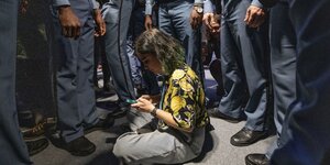 Eine Frau mit Handy sitz zu Füßen von Sicherheitskräften