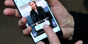 Eine Hand hält ein Smartphone, auf dem eine Frau zu sehen ist.