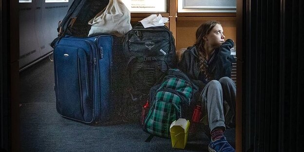 Greta Thunberg sitzt auf dem Boden eines Zuges der Deutschen Bahn. Um sie herum stehen Koffer und Taschen und eine Box von einem Imbiss.