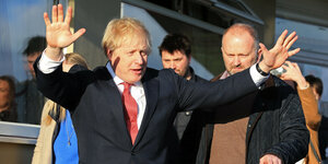 Boris Johnson bei seinem Besuch in Sedgefield. Er steht draußen und heb beide Arme in die Luft. Er trägt einen Anzug. Im Hintergrund stehen Menschen.