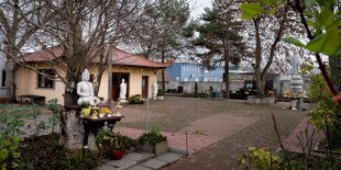 Pagode in Berlin-Lichtenberg: Ein kleines, eingeschossiges Haus mit geschwungenem Dach und kleinem Garten. Davor sitzt eine Buddha-Statue.