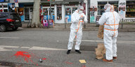 Zwei Männer in weißen Schutzanzügen stehen auf einer Straße in Hamburg. Auf dem Boden ist rote Farbe