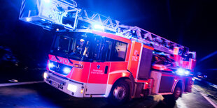 Ein Drehleiterwagen der Feuerwehr fährt mit Blaulicht an einer Unfallstelle vorbei.