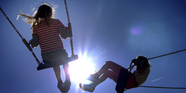 Zwei Kinder schaukeln vor blauem Himmel.