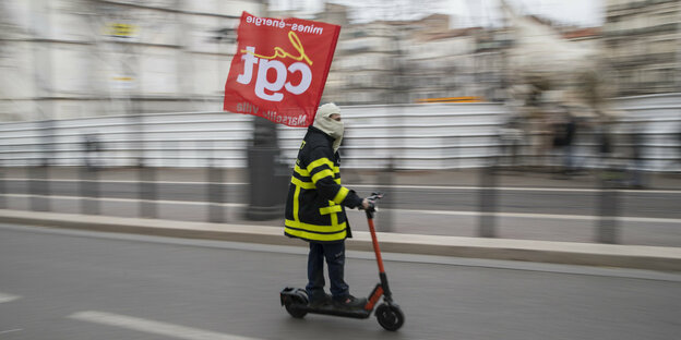 Ein Demonstrant fährt mit dem Roller die Straße entlang und hält dabei eine Fahne des Gewerkschaftsbunds CGT