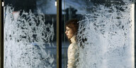 Eine Frau steht hinter einer Glastür, die mit Eisblumen bedeckt ist.