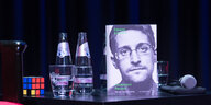 Ein Tisch mit einem Zauberwürfel, einem Mikro, Wasserflaschen und Edward Snowdens Buch