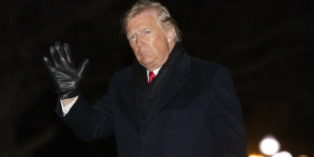 Donald Trump ist draußen im Dunklen zu sehen und erhebt eine behandschuhte Hand zum Gruß