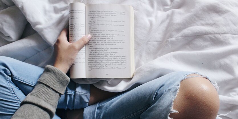 Mensch sitzt im Schneidersitz auf dem Boden und liest ein Buch