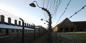 Ein Stacheldrahtzaun und Gebäude im ehemaligen NS-Vernichtungslager Auschwitz