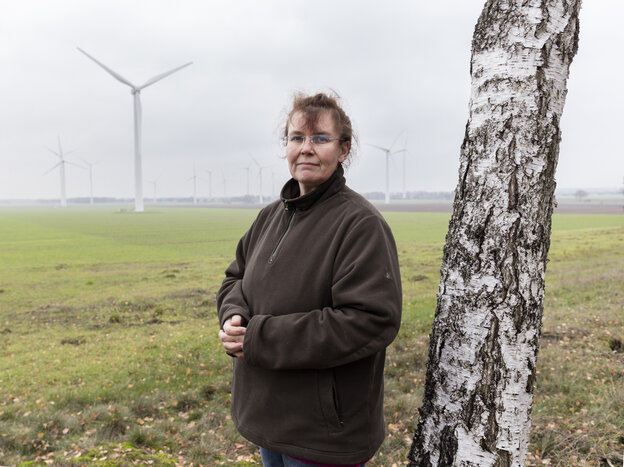 Eine Frau steht an einem Baum, dahinter Landschaft mit Windrad