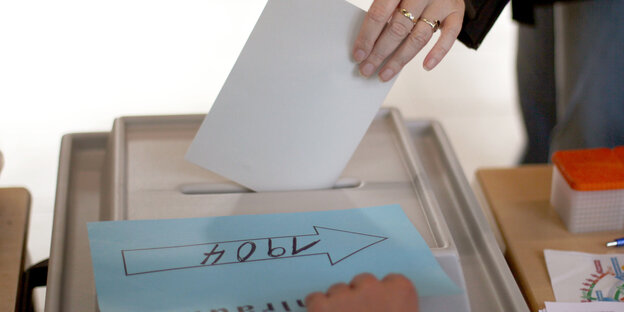 Eine Hand mit Stimmzettel über einer Wahlurne
