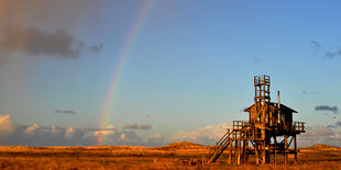 rechts eine Holzhütte, links weiter Himmel mit Regenbogen