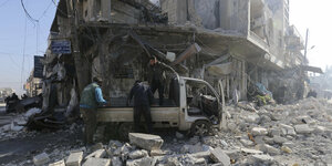 Drei Männer steigen von oder stehen um dier Ladefläche eines Wagens inmitten von Trümmern