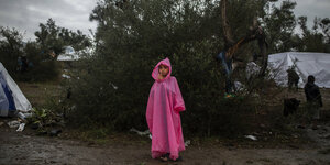 Ein kleines Mädchen in einem rosafarbenen Regenumhang steht verloren in einer regnerischen Landschaft