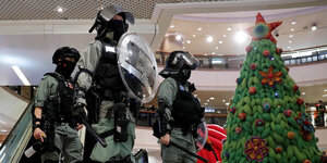 Drei behelmte und mit Schlagstöcken bewaffnete Polizisten neben einem Weihnachtsbaum in einer Shopping Mall