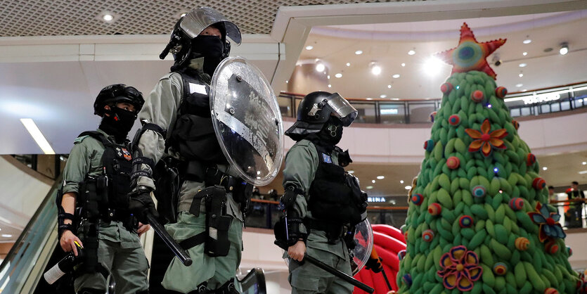 Drei behelmte und mit Schlagstöcken bewaffnete Polizisten neben einem Weihnachtsbaum in einer Shopping Mall