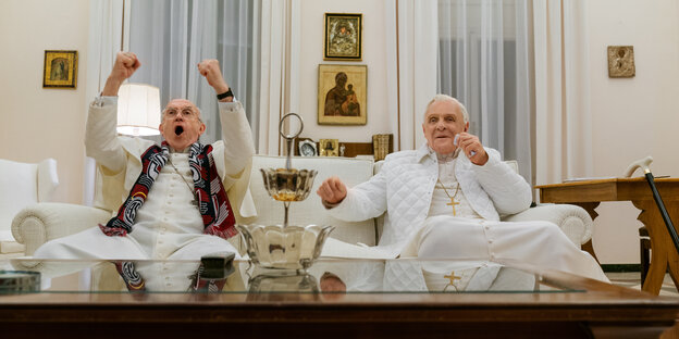 Die zwei Papst-Darsteller sitzen auf einer Couch, die Figur des Franziskus verfällt in Fußballtorjubel