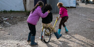 In einem Flüchtlingslager spielen drei Kinder mit einem Fahrrad