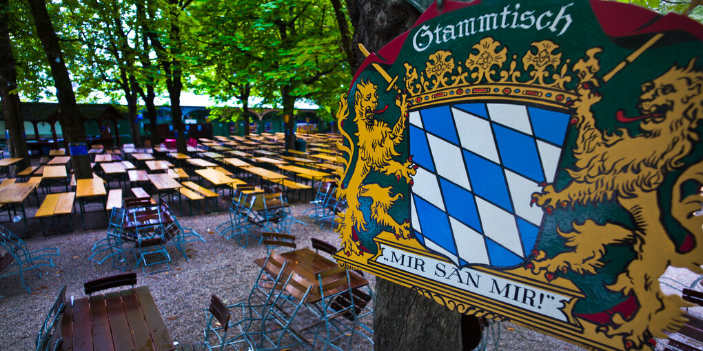 Blick auf einen leeren Biergarten, im Vordergrund ein Schild mit der Aufschrift "Stammtisch - Mir san mir!"