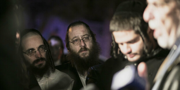 Orthodoxe Juden stehen um einen Mann, der vor einem Mikrophon spricht.
