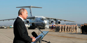 Wladimir Putin im profil, im Hintergrund ein Flugzeug und Soldaten
