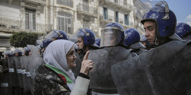 Eine ältere Frau steht vor einer Reihe von Polizisten mit Schutzkleidung