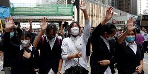 Fünf Frauen mit weißen Röcken und Atemschutzmasken heben die Hand zum Protest während einer Demonstration in Hongkong