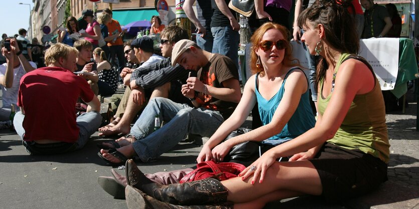 Menschen sitzen im Sommer an einem Bordstein