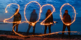 Vier Leute malen mit Wunderkerzen die Zahl 2020 in die Luft, dahinter die Ostsee