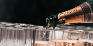 Aus einer Flasche, auf der Champagner steht, wird selbiger in Gläser gegossen