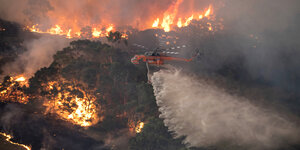 Ein Hubschrauberfliegt über einen brennenden Wald und löscht.