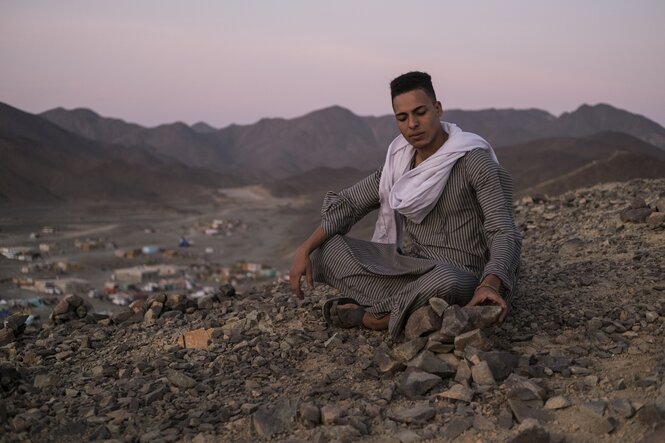 ein Mann sitzt traditionellem Gewand im Schneidersitz auf einem Berg