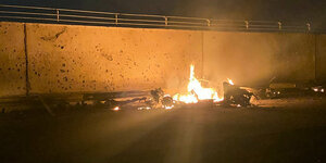 Brennendes Fahrzeugwrack vor einer Mauer - in der Nachtder