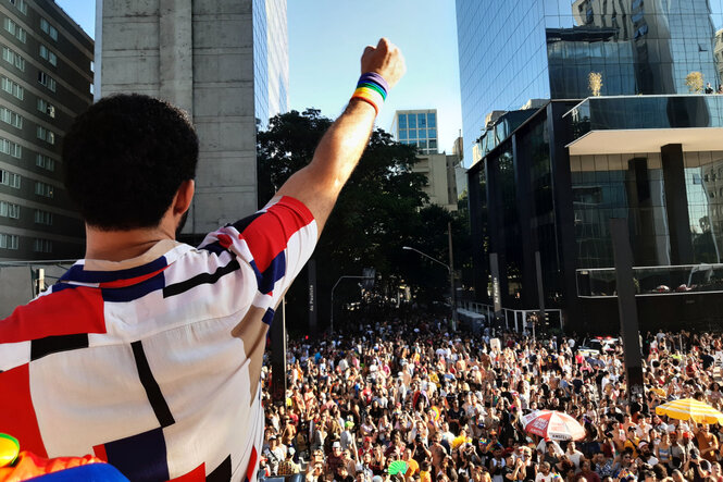 David Miranda von hinten fotografiert, reckt die rechte Faust hoch und blickt auf die Sao Paulo Pride Parade