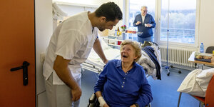 Ein Mann in weißer Kleidung spricht mit einer Patientin im Rollstuhl