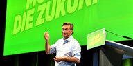 Redner im kurzärmeligen Hemd vor einer grünen Wand