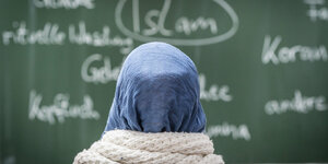 Eine Schülerin mit Kopftuch sitzt in einer Schule bei einer Unterrichtsstunde zum Thema Islam vor einer Tafel.