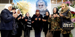 Acht iranische Frauen mit Kopftuch halten die Hände offen vor sich zum Gebet für den getöteten General Soleimani, der auf einem Plakat hinter der Gruppe zu sehen ist