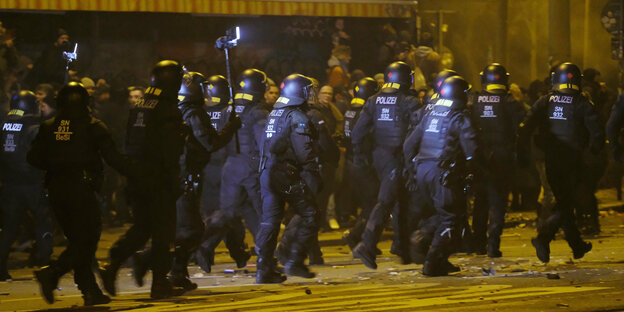 Polizisten rennen im Stadtteil Connewitz in Leipzig auf der Straße. Sie tragen Schutzmontur.