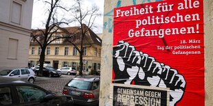 ein rotes Plakat mit stilissierten gereckten Fäusten klebt auf einer Hauswand