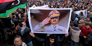 Menschen tragen ein Plakat mit dem Foto eines Generals
