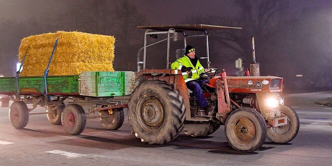 Ein Bauer auf seinem Traktor, der einen mit Stroh beladener Anhänger zieht