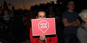 Eine Frau hält ein rotes Schild mit der Aufschrift Adani