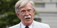 John Bolton spricht in hellem Anzug vor unscharfem Hintergrund