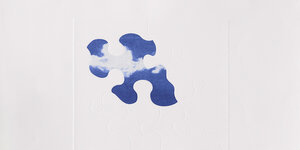 Das Kunstwerk von Yoko Ono zeigt ein Puzzle mit wenigen Puzzleteilen. Die äußeren Puzzleteile sind weiß. Nur ein Teil in der Mitte ist farbig. Es zeigt einen blauen Himmel mit weißen Wolken.