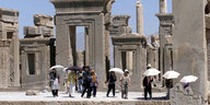Touristen und Touristinnen schützen sich mit Regenschirmen vor der Sonnen vor den Ruinen der antiken Stadt Persepolis
