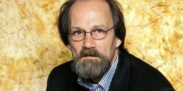 Portrait von Horst Röper vor goldenem Hintergrund. Röper hat etwas längere Haare, eingefallene Wangen und einen Bart. Er trägt eine kleine ovale Brille.